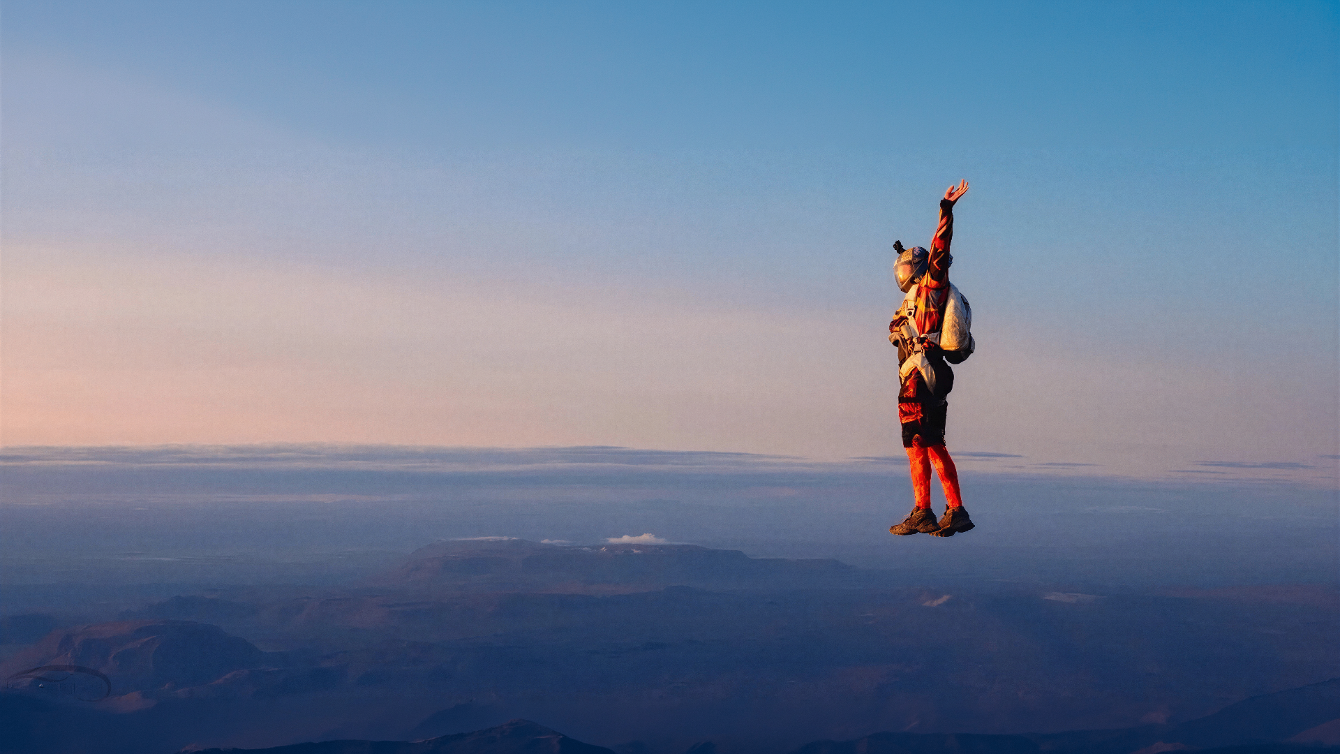 Solo skydiver in a red suit suspended in freefall above Iceland's volcanic mountains at sunset