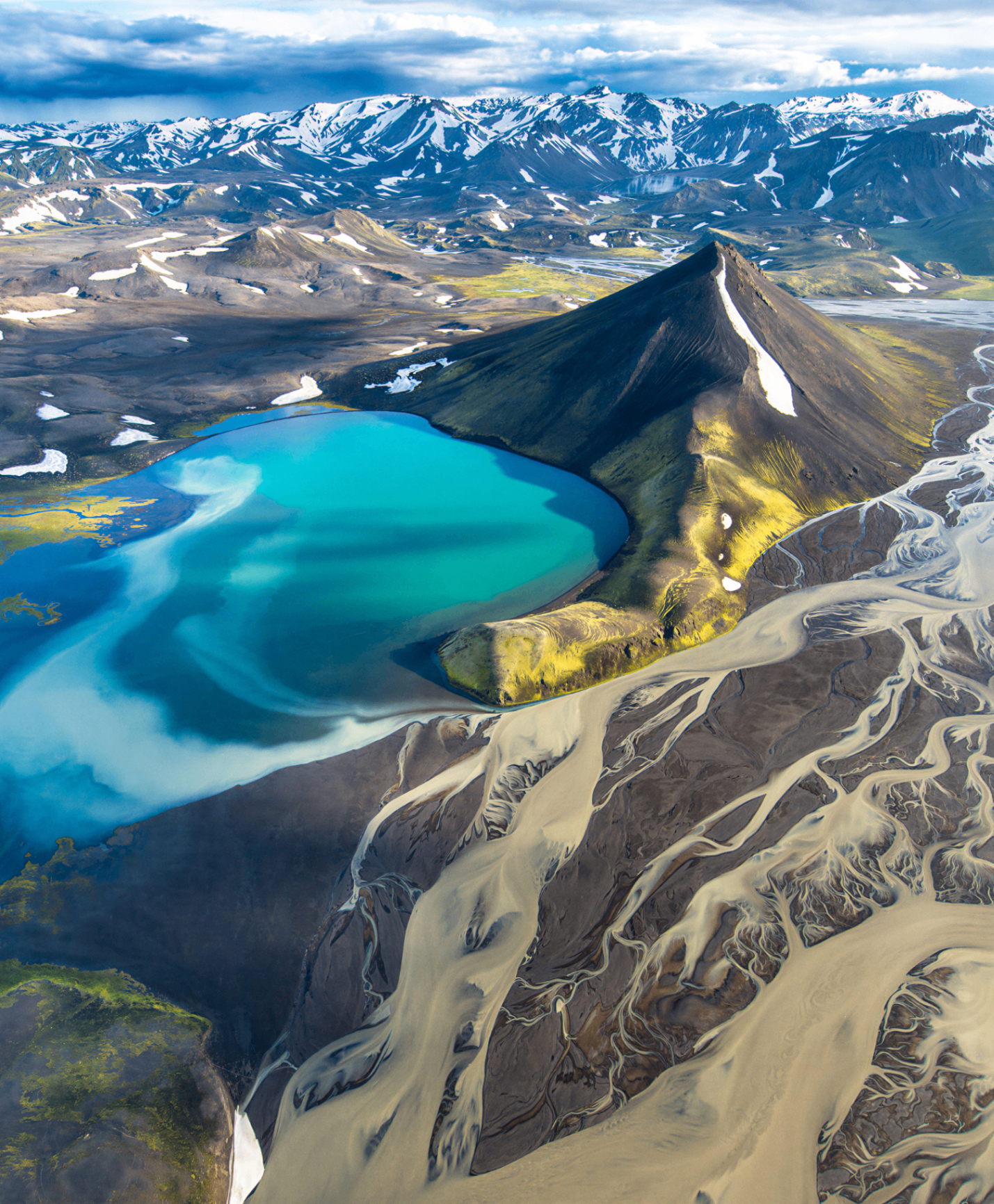 Aerial view of Iceland's vivid turquoise glacial lake surrounded by volcanic mountains and snow-capped peaks