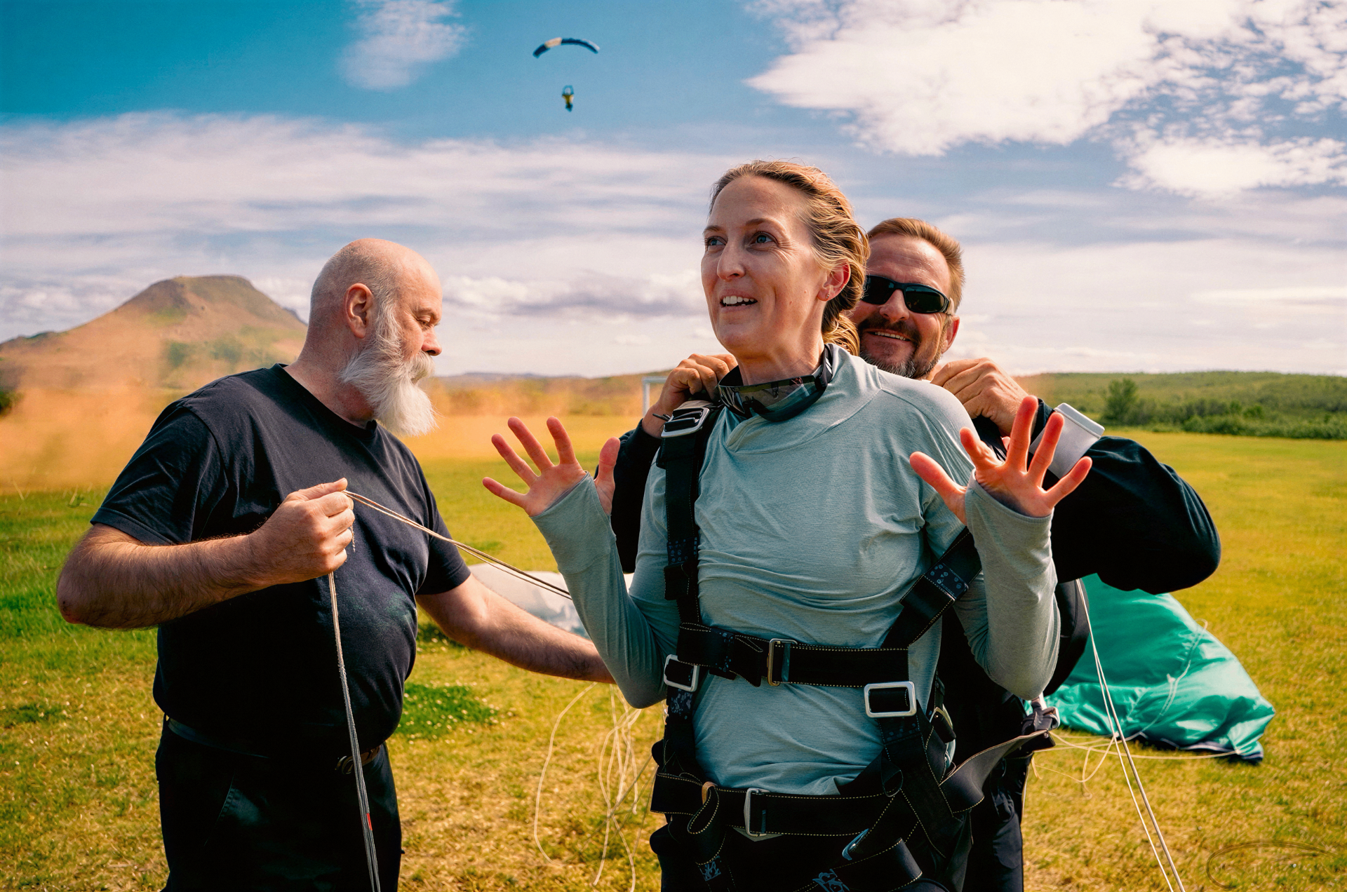 Tandem skydiver celebrating on the grass after landing, with instructor and canopy in the Icelandic countryside